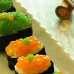 Colorful Tobiko Sushi roll with bright orange flying fish eggs sprinkled on top, showcasing vibrant sushi presentation with salmon, cucumber, and nori.